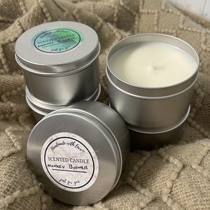 May include: Two silver tin candle jars with white lids. The labels on the jars say "Handmade with love" and "Scented Candle Monkey Business just for you".