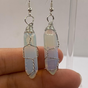 May include: A pair of silver wire wrapped earrings with white opal stones. The earrings are dangling and have a simple design.