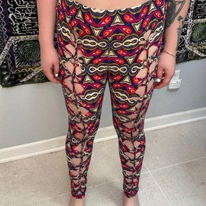 May include: Leggings with a colorful geometric pattern in red, blue, yellow, and white. The leggings have cut-out details along the sides. The model is wearing a black bra.