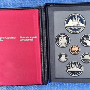 Può includere: Un set di monete della Royal Canadian Mint in una custodia nera con interno rosso. Il set include sette monete color argento e rame con immagini canadesi, tra cui un dollaro, 50 centesimi, 25 centesimi, 10 centesimi, 5 centesimi e un penny.