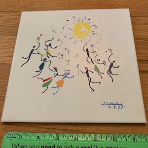 Pu&ograve; includere: Una piastrella di ceramica bianca con un'illustrazione colorata disegnata a mano di persone che ballano intorno a un sole giallo. La piastrella &egrave; firmata "2.7.59."