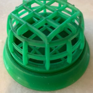 May include: A green plastic floral frog, also known as a flower holder, with a grid-like top and a circular base. The flower arranging tool is designed to hold flower stems in place for floral arrangements.