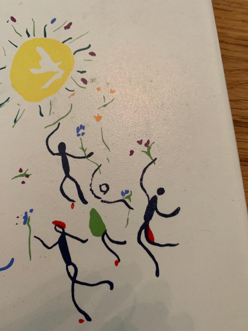 Pu&ograve; includere: Uno sfondo bianco con un sole giallo che contiene una colomba bianca. Ci sono quattro figure di bastoncino in nero, blu e rosso, che ballano intorno al sole. Le figure tengono fiori blu, rossi e verdi.