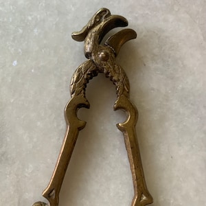 May include: A brass nutcracker shaped like a bird with intricate details. The bird's head is open, revealing the nutcracker's jaws.
