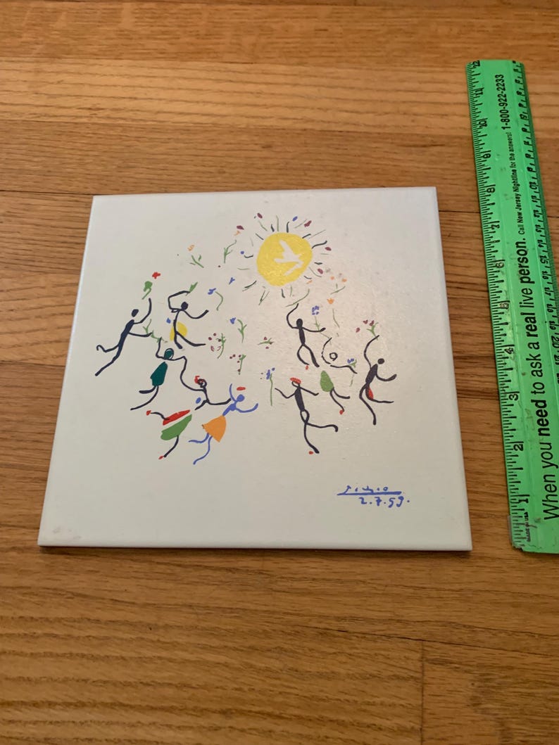 Pu&ograve; includere: Una piastrella di ceramica bianca con un'illustrazione colorata disegnata a mano di persone che ballano intorno a un sole giallo con una colomba bianca. La piastrella &egrave; firmata "2.7.59."
