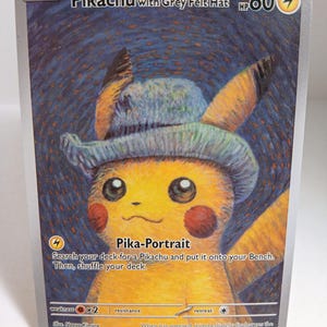 May include: A Pokémon trading card featuring Pikachu wearing a grey felt hat. The card has the text "Pikachu with Grey Felt Hat" and "Pika-Portrait". The card has a yellow Pikachu with red cheeks and a blue background.