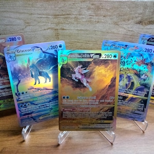 May include: Five holographic Pokémon trading cards displayed on clear stands. The cards feature various Pokémon characters, including Glaceon, Palkia, and Mewtwo, with vibrant colors and dynamic artwork. Each card has a VSTAR symbol and a numerical value.