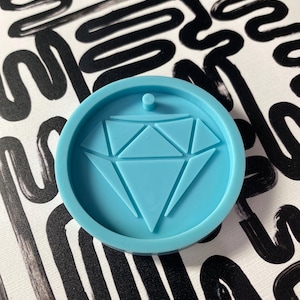 May include: A light blue silicone mold with a diamond shape in the center. The mold is round and has a hole at the top for hanging.