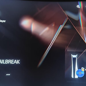 May include: A dark screen displaying the PS5 interface. The text "PS5 AUTO JAILBREAK" is visible, along with options for "Play" and "Disc Player." The time 12:14 AM is displayed in the upper right corner. A stylized graphic of a console is also present.