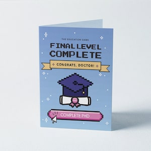 Könnte beinhalten: Gefaltete Grußkarte mit Pixel-Design. Die Karte hat einen blauen Hintergrund mit dem Text "THE EDUCATION GAME FINAL LEVEL COMPLETE" und "CONGRATS, DOCTOR!". Eine pixelige Doktorhut und eine Urkunde sind ebenfalls abgebildet.