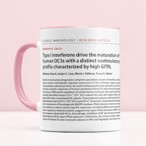 May include: A white ceramic mug with a pink handle and rim. The mug features text from a research article on immunology, including the title "Type I interferons drive the maturation of human DC3s". The mug is set against a light pink background.