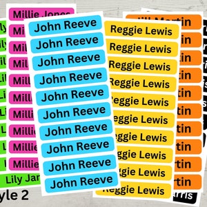 May include: A set of colorful name labels with different names printed on them. The labels are in various colors, including green, pink, blue, yellow, and orange. The text on the labels is black. The labels are arranged in rows and columns. The text "Style 2" is printed at the bottom of the image.