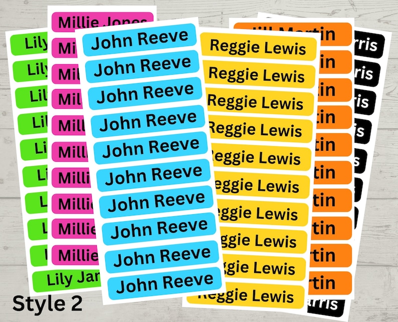 May include: A set of colorful name labels with different names printed on them. The labels are in various colors, including green, pink, blue, yellow, and orange. The text on the labels is black. The labels are arranged in rows and columns. The text "Style 2" is printed at the bottom of the image.