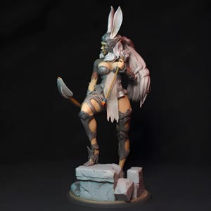 May include: A white rabbit-eared figurine of a female warrior wearing silver armor and holding a bow and arrow. The figurine is standing on a stone base.