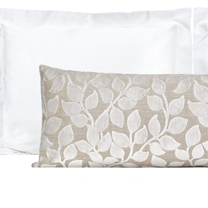 May include: A pair of decorative pillows, one white and one with a beige background and a white leaf pattern.