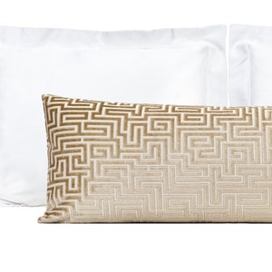 May include: A brown and white patterned lumbar pillow with a geometric design. The pillow is on a white bed.