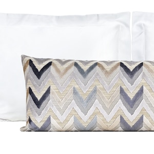 May include: A decorative throw pillow with a chevron pattern in shades of gray, beige, and brown. The pillow is on a white background.