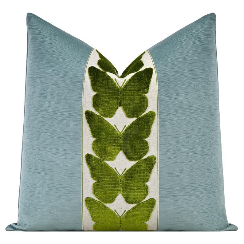 May include: A light blue cushion with a textured surface. A central panel features green butterfly motifs on a white background. The cushion has a soft, plush appearance and a classic shape, suitable for a sofa or bed.