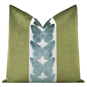 May include: A decorative pillow with a textured olive green background and a central panel featuring teal butterfly appliques. The pillow has a soft, plush appearance, adding a touch of nature-inspired elegance to home decor.