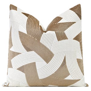 May include: A decorative throw pillow with a geometric pattern in shades of brown and white. The pillow features a woven design with raised lines.