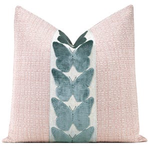 May include: A decorative throw pillow with a textured, light pink fabric. A vertical band of off-white fabric runs down the center, featuring embroidered teal butterfly designs. The pillow has a soft, inviting appearance.