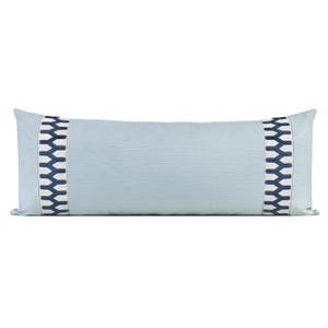 May include: A long rectangular lumbar pillow in a solid light blue fabric with a subtle horizontal texture. The pillow features two vertical bands of cream-colored fabric with a dark navy blue geometric chevron pattern on each side.