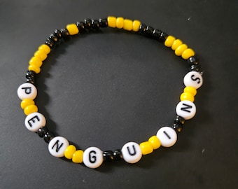 May include: A black and yellow beaded bracelet with the word "PENGUINS" spelled out in white beads.