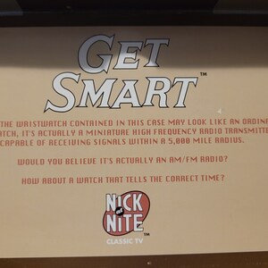 May include: A tan cardboard box with the words "GET SMART" in large white letters. The box also features the text "ALTHOUGH THE WRISTWATCH CONTAINED IN THIS CASE MAY LOOK LIKE AN ORDINARY WRISTWATCH, IT'S ACTUALLY A MINIATURE HIGH FREQUENCY RADIO TRANSMITTER CAPABLE OF RECEIVING SIGNALS WITHIN A 5,000 MILE RADIUS. WOULD YOU BELIEVE IT'S ACTUALLY AN AM/FM RADIO? HOW ABOUT A WATCH THAT TELLS THE CORRECT TIME?" and a red and white logo that says "NICK AT NITE" with the text "CLASSIC TV" below it.