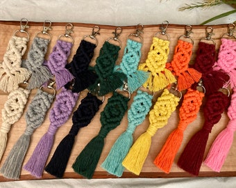 May include: A collection of 12 colorful macrame keychains with tassels. The keychains are made with different colored cords and feature a variety of knot patterns.