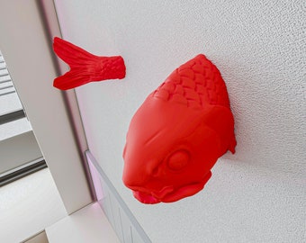 May include: A red fish sculpture with a textured surface, mounted on a white wall.