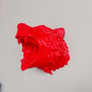 May include: A bright red 3D printed sculpture of a wolf's head with its mouth open in a snarl. The sculpture is detailed with sharp teeth and textured fur.