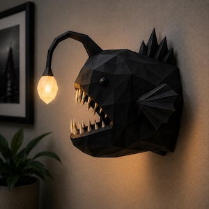 May include: A black, geometric, low-poly anglerfish wall lamp featuring a faceted surface, sharp pointed teeth, and a protruding lure with a glowing, translucent, diamond-shaped light bulb extending from the top of its head.