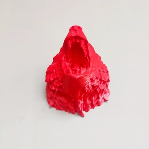 May include: A bright red 3D printed sculpture of a wolf's head with its mouth open in a ferocious snarl. The sculpture is detailed with sharp teeth and textured fur.