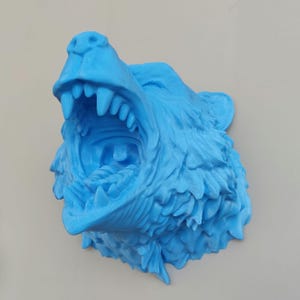 May include: A 3D printed blue wolf head sculpture with an open mouth and sharp teeth. The sculpture is made of a textured material and has a realistic appearance.