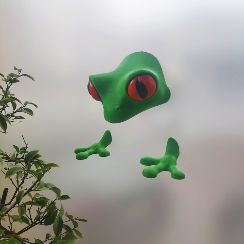 May include: Green frog wall decor with large red eyes and a 3D design. The frog has two arms and two legs.