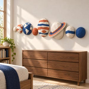 Può includere: Un set di otto decorazioni murali geometriche low-poly che rappresentano pianeti e corpi celesti in tonalità di blu, arancione e bianco. La collezione include forme sferiche e dotate di anelli con superfici sfaccettate, disposte orizzontalmente.