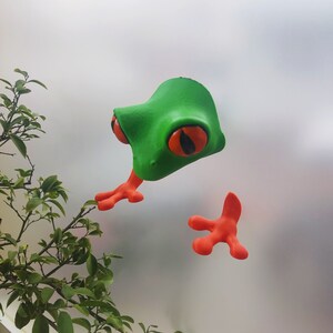 May include: A green and orange frog figurine with large eyes. The frog is made of plastic and has a textured surface.