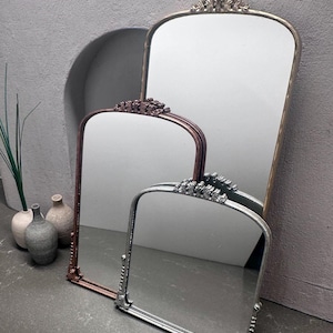 May include: Three decorative mirrors with ornate frames in gold, bronze, and silver. The mirrors have a rectangular shape with a curved top and are arranged against a neutral grey background. The frames feature detailed floral and scrollwork.