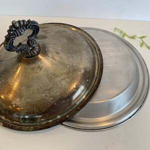 Puede incluir: Un plato de servir plateado con tapa. La tapa tiene un asa decorativa. El plato es de metal y tiene un acabado brillante.