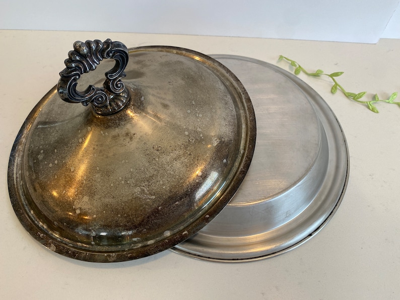 Puede incluir: Un plato de servir plateado con tapa. La tapa tiene un asa decorativa. El plato es de metal y tiene un acabado brillante.