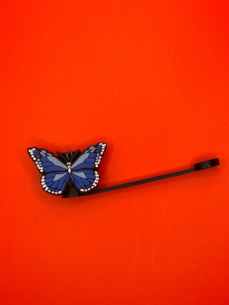 Pu&ograve; includere: Un tappo per bottiglia a forma di farfalla blu con un anello di metallo nero. La farfalla ha accenti bianchi ed &egrave; attaccata a un anello di metallo nero.