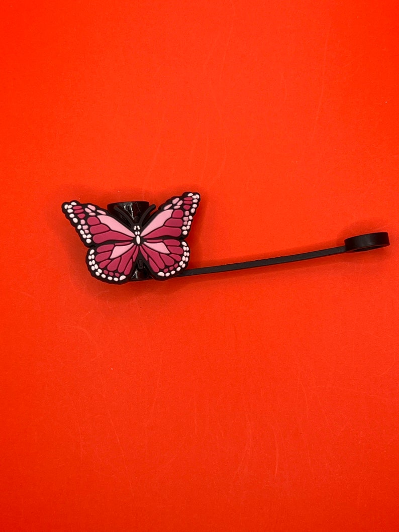 Pu&ograve; includere: Un tappo per bottiglia a forma di farfalla nero e rosa con uno spago nero attaccato.