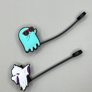 May include: Two black ghost-shaped phone charms with different expressions. One ghost is wearing red sunglasses and is giving a thumbs up. The other ghost is covering its face with its hands.