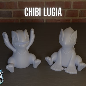 Op de afbeelding: Twee witte, 3D-geprinte, chibi-stijl Lugia Pokémon-figuurtjes. Eén figuurtje zit met zijn armen omhoog, terwijl de andere zit met zijn armen naar beneden. De tekst "CHIBI LUGIA" is in het zwart bovenaan de afbeelding gedrukt.