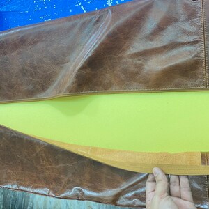 May include: A brown leather bag with a zipper opening and a yellow foam lining. The bag has a brown strap and a brown elastic band.