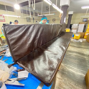 May include: A brown leather bench cushion with a slightly rounded edge. The cushion is in a workshop setting.