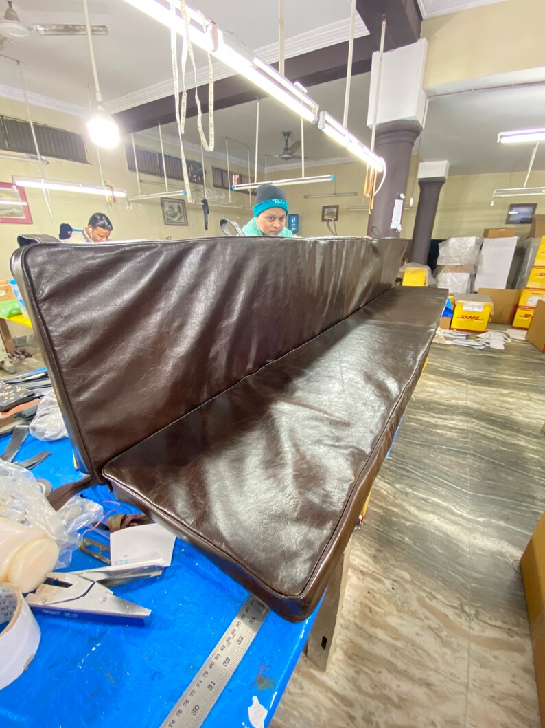 May include: A brown leather bench cushion with a slightly rounded edge. The cushion is in a workshop setting.