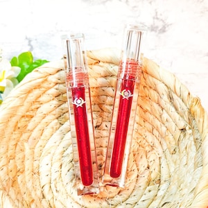 May include: Two clear glass tubes with red liquid inside, sitting on a woven straw basket. The tubes have a silver cap and a silver band around the middle.