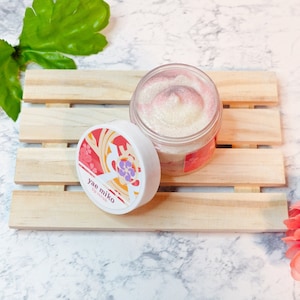 May include: A white jar with a pink and white swirl lip scrub. The jar has a white lid with a floral design and the text "yae miko lip scrub". The jar is sitting on a wooden tray.