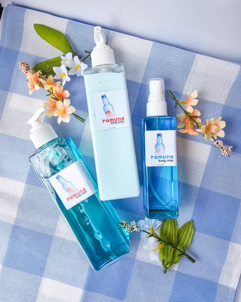Pode incluir: Tr&ecirc;s garrafas de produtos para o cuidado do corpo sobre uma superf&iacute;cie quadriculada azul e branca. As garrafas s&atilde;o transparentes e cont&ecirc;m l&iacute;quido azul. As garrafas s&atilde;o etiquetadas como "ramune body lotion", "ramune body mist" e "ramune body wash".